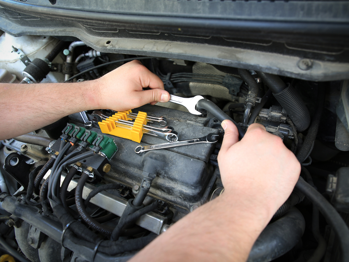 Hands using a wrench on a car engine with yellow tool case nearby