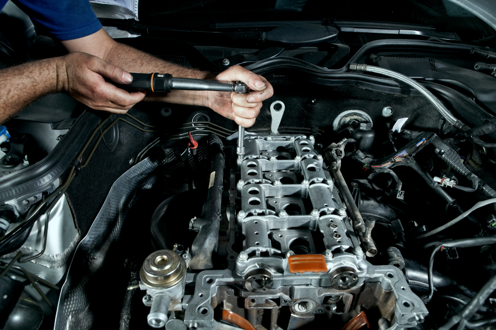 Mechanic using a torque wrench on a car engine in an open hood compartment
