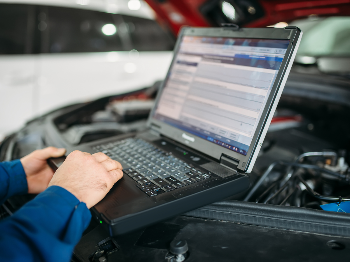 Mechanic using a laptop to diagnose a car engine in a garage