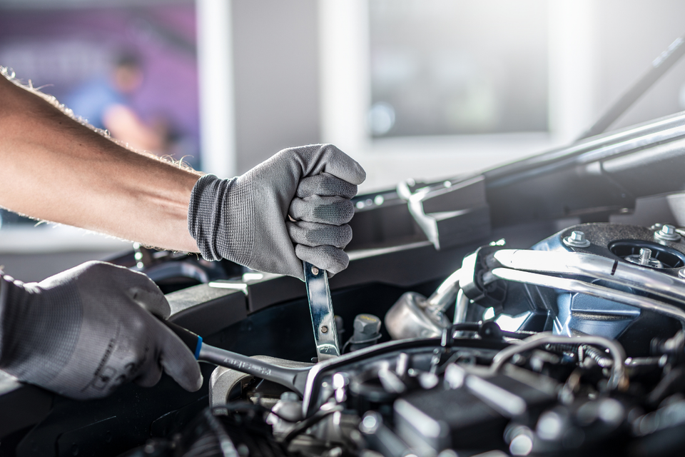 Mechanic wearing gloves checks a car engine with a wrench in a garage