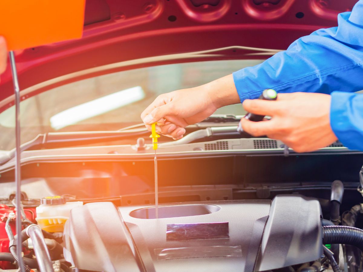 Mechanic checking engine oil with a dipstick under a car hood, close-up with blue gloves