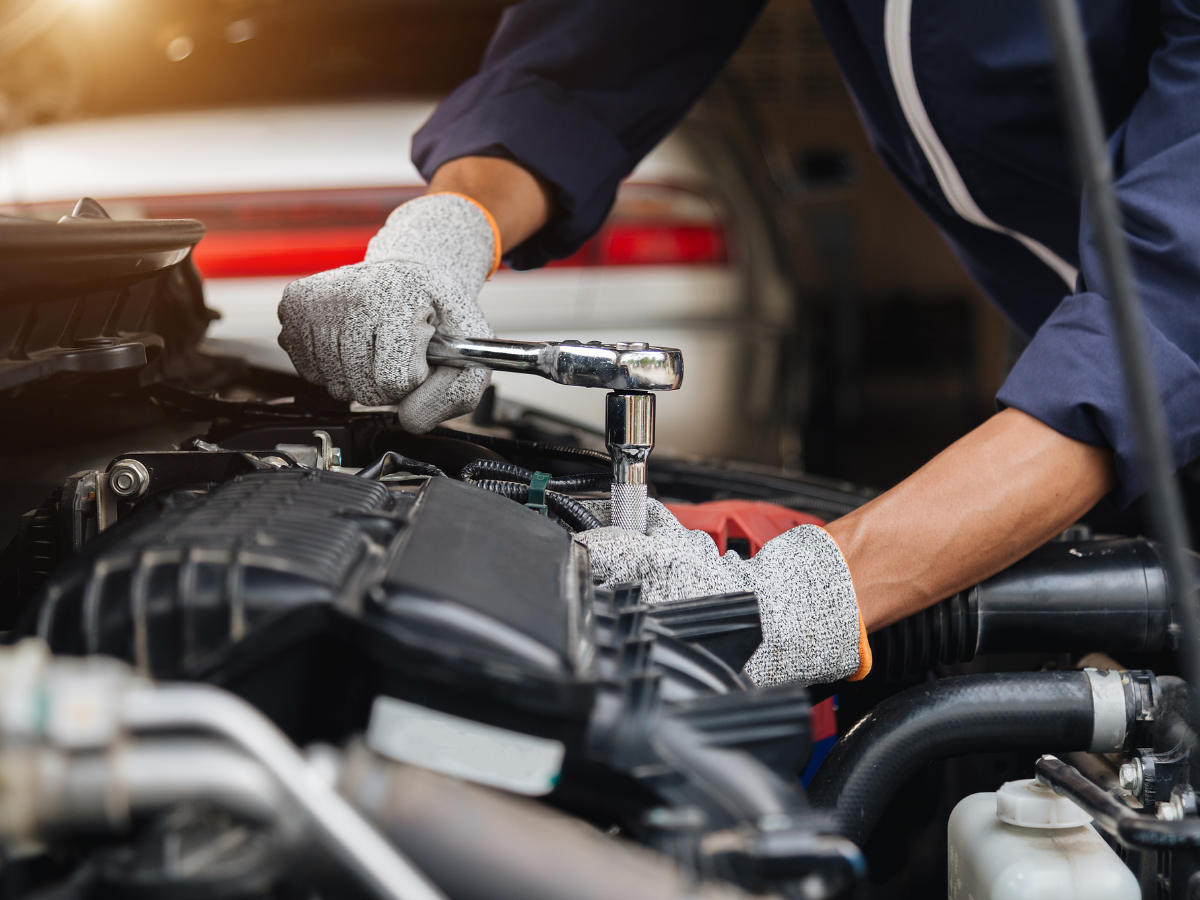 Mechanic tightening a bolt in a car engine bay with a socket wrench, wearing gray work gloves