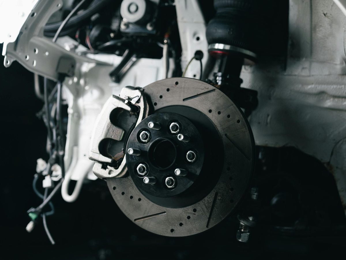 Close-up of a car brake rotor and caliper in a garage, with metal tools and machinery in the background