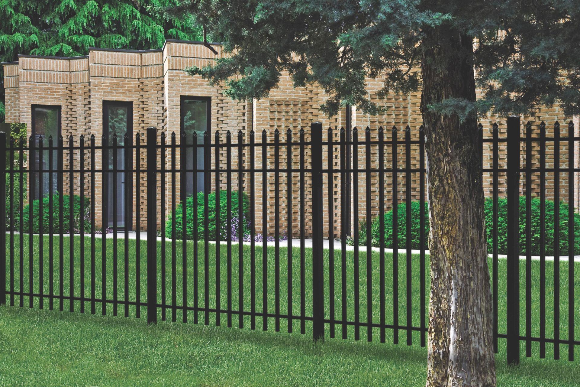 Black metal fence in front of a brick building with a tree in the foreground.