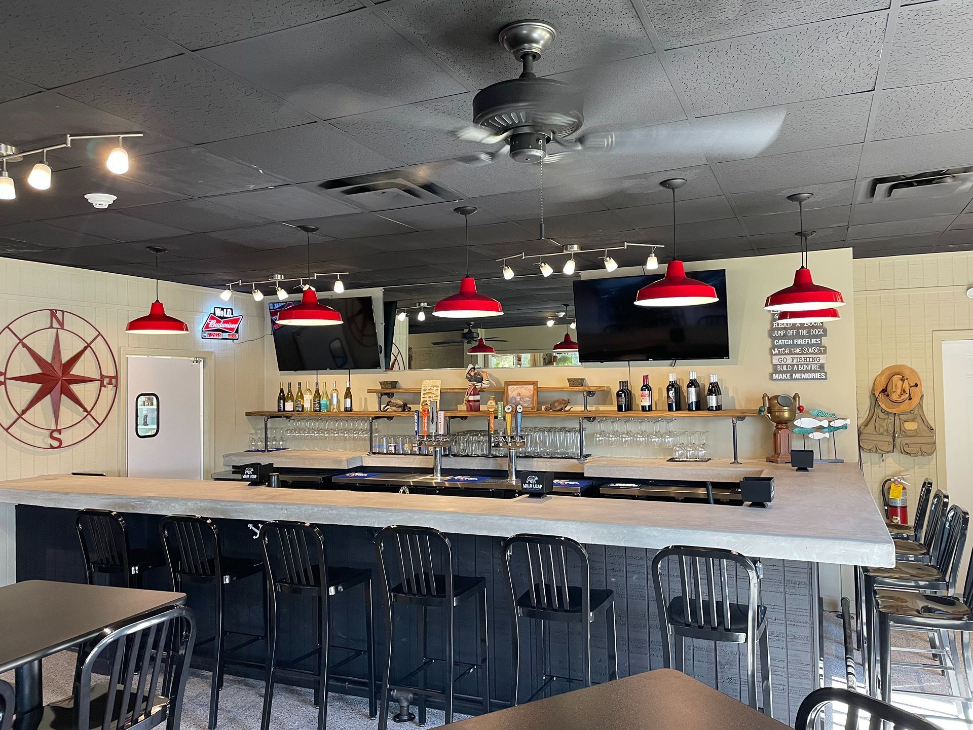 Bar interior with black chairs, concrete bar, red pendant lights, compass rose wall decor.
