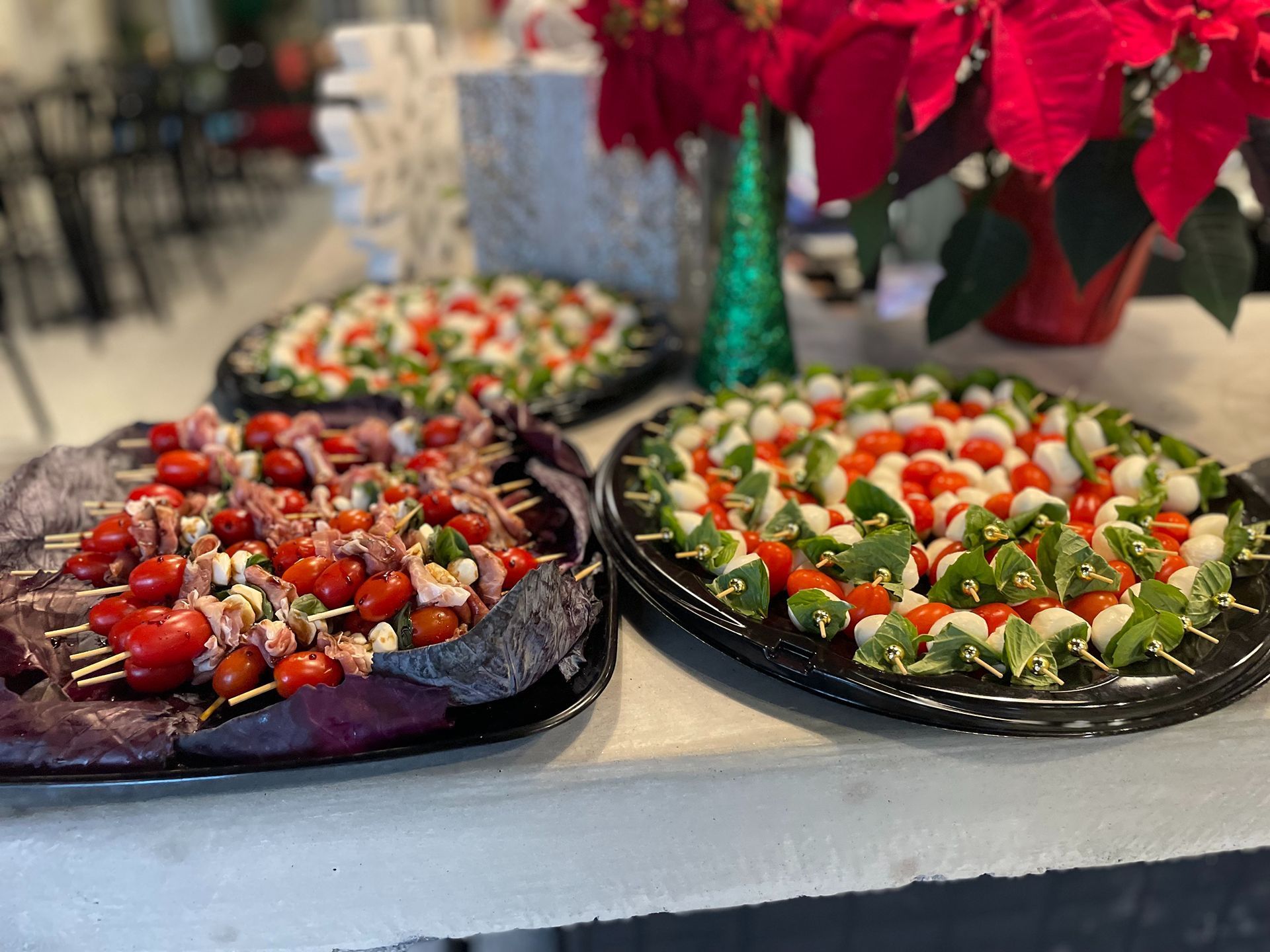 Appetizer skewers: tomato, mozzarella, basil and meat, arranged on platters, with poinsettia in background.