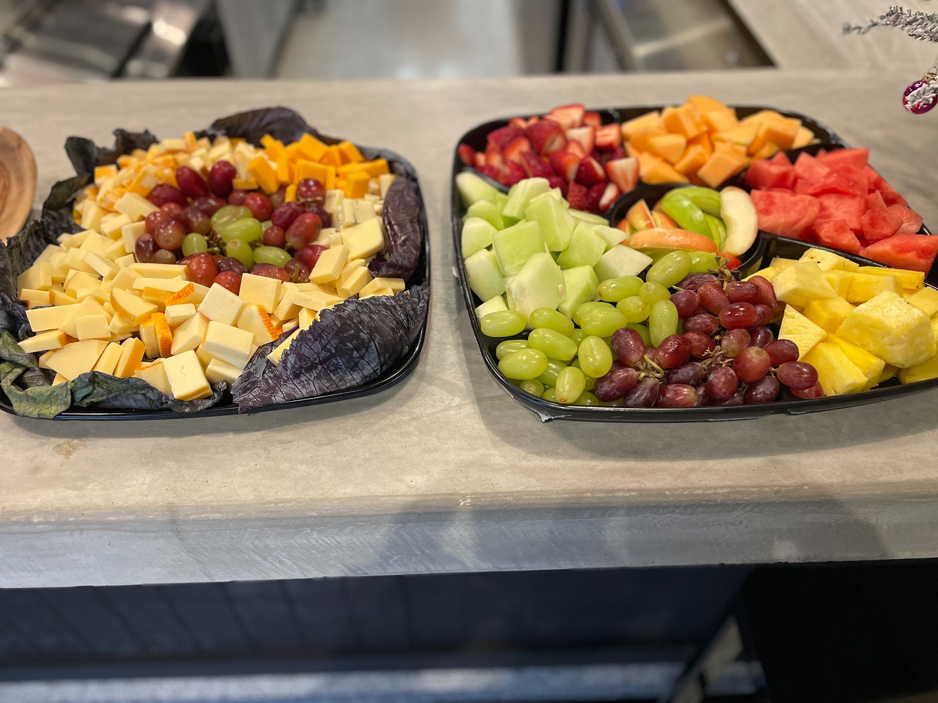 Two platters with cheese and grapes, and fruit like watermelon, pineapple, and grapes.