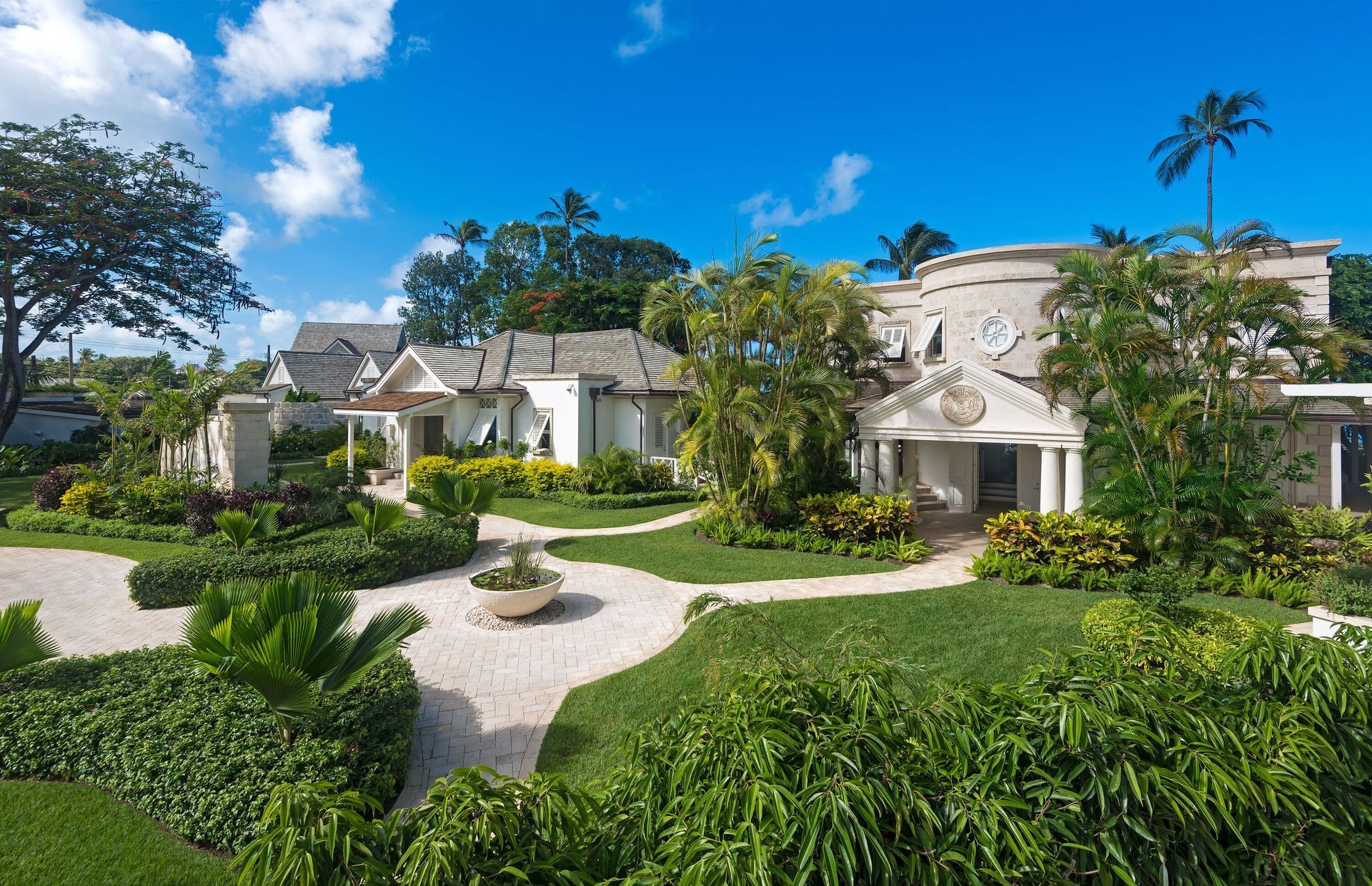 Lush green garden with white buildings and a clear blue sky.