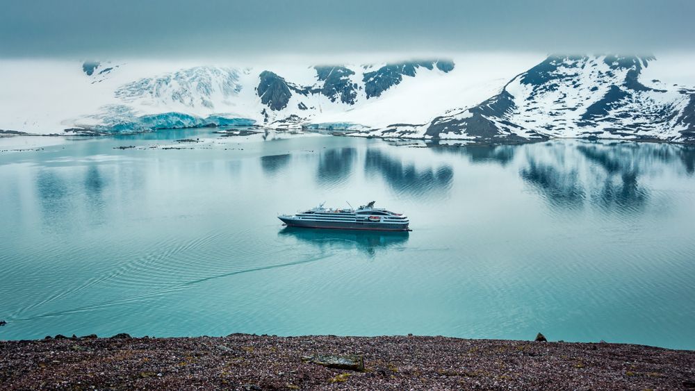 Snowy mountains reflected in calm Arctic water with a small boat in the center