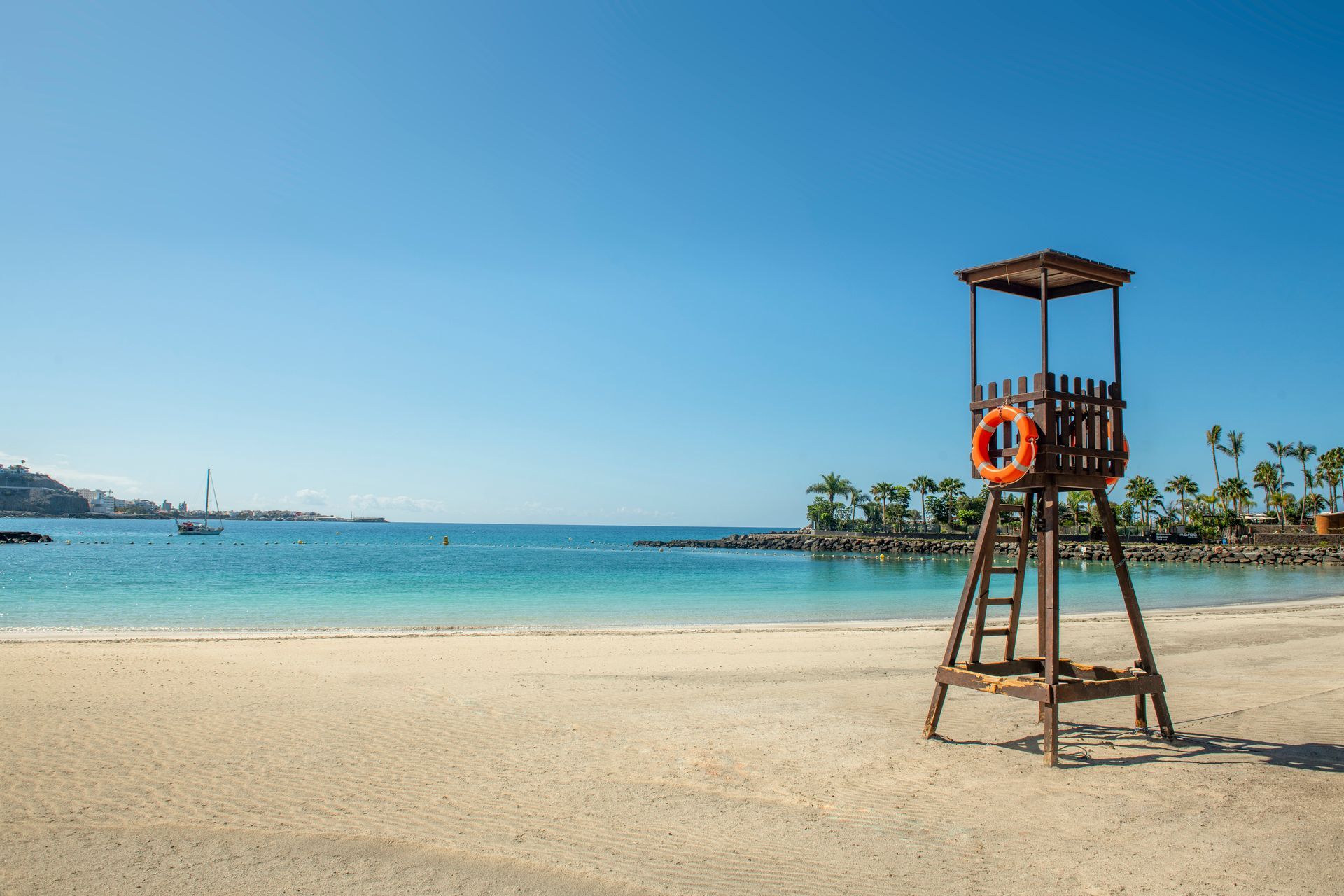 Sandy beach with a lifeguard tower, blue sea, and clear sky on a sunny day. Anfi Beach, Gran Canaria