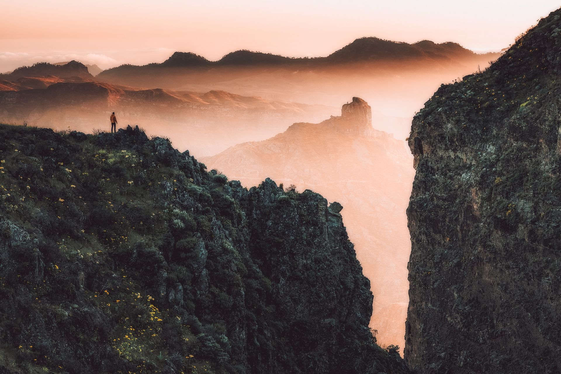 Misty mountain peaks at sunrise with dark rocky cliffs in the foreground