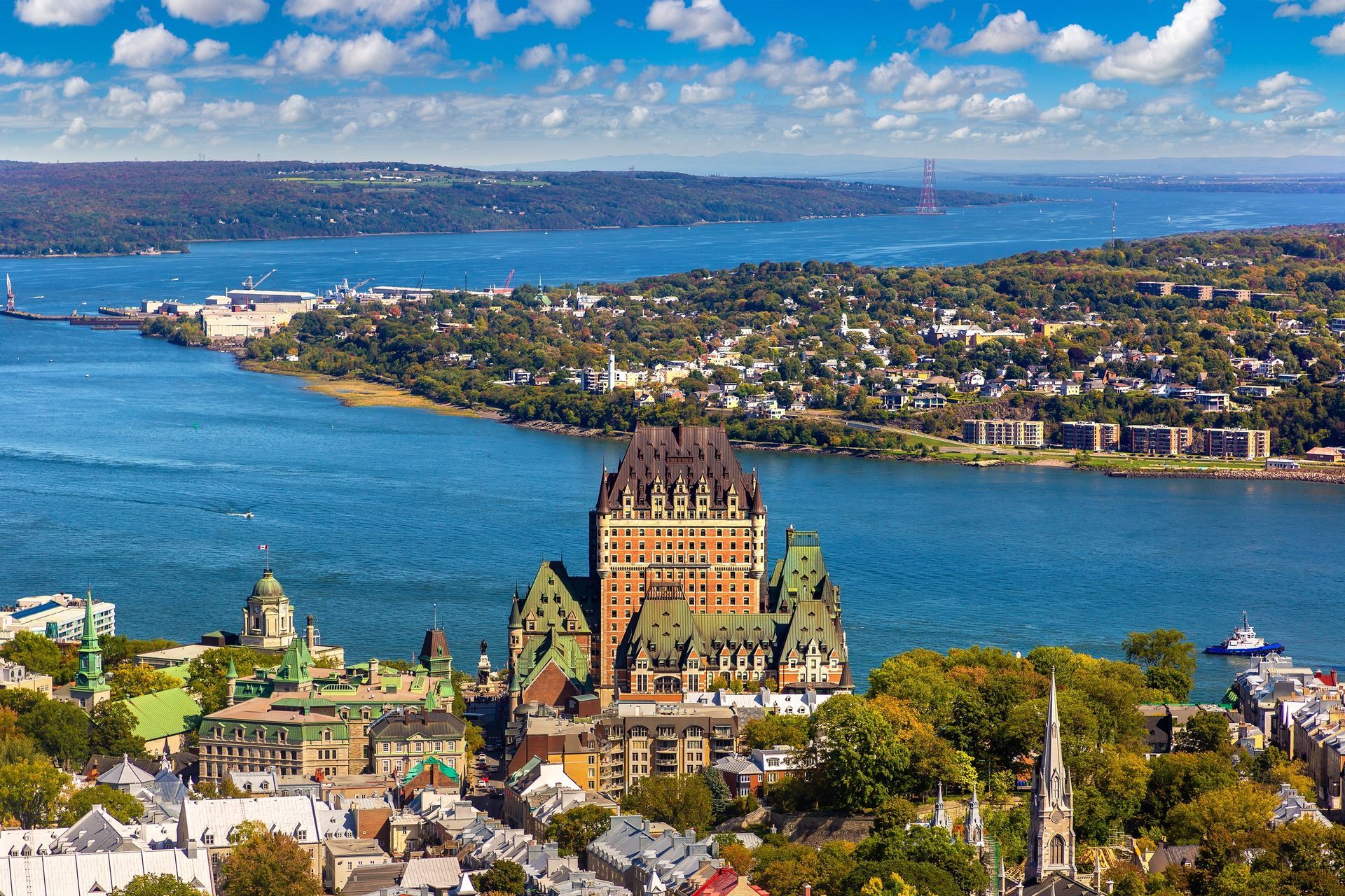 Aerial view of Quebec City, Canada, with Château Frontenac dominating the skyline, blue river, and green trees.