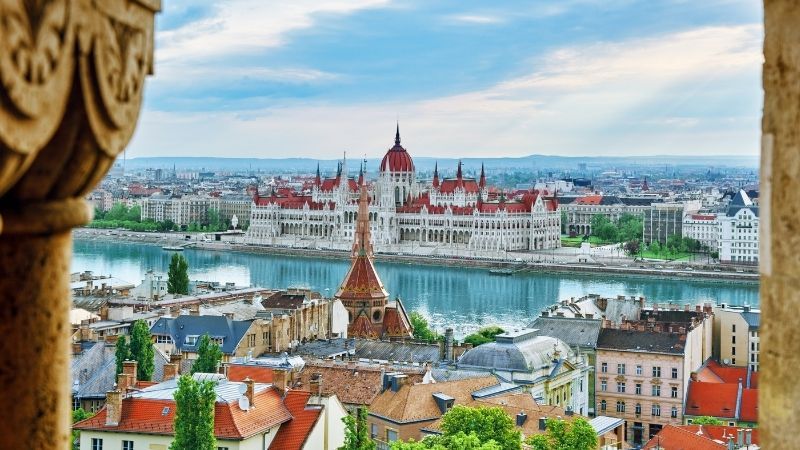 Panoramic cityscape with a river, red-roofed buildings, and a grand domed parliament across the water