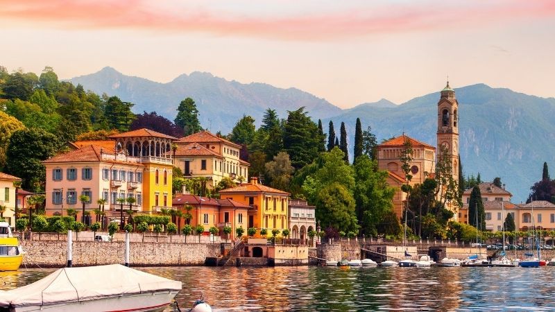 Colorful lakeside village with boats, church tower, and mountains at sunset