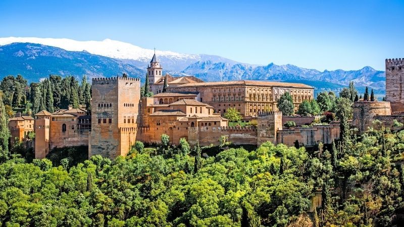 Historic palace complex amid lush trees with mountains and a blue sky in the background