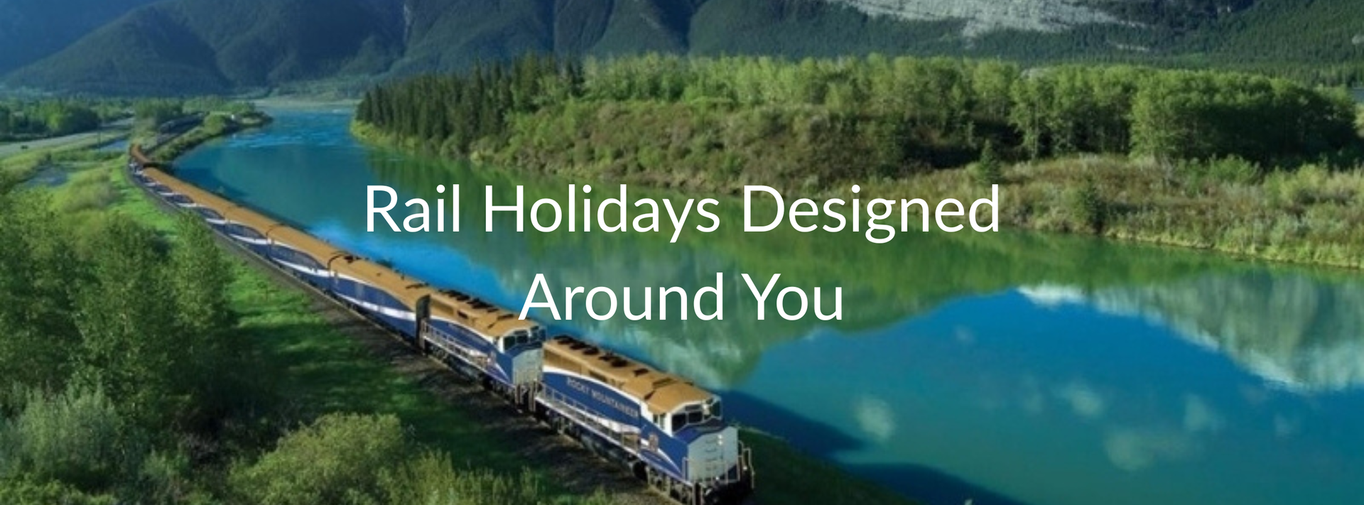 Train curving beside a turquoise river with pine forest and snowcapped mountains in the background