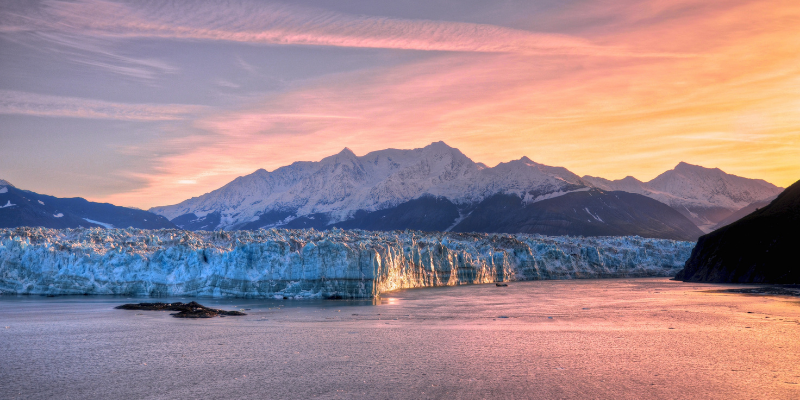 Snowy mountains and glacier at sunset over a calm pink-blue bay.