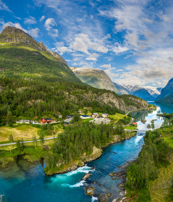 Bright mountain valley with a turquoise river, green forest, and small village under a cloudy blue sky