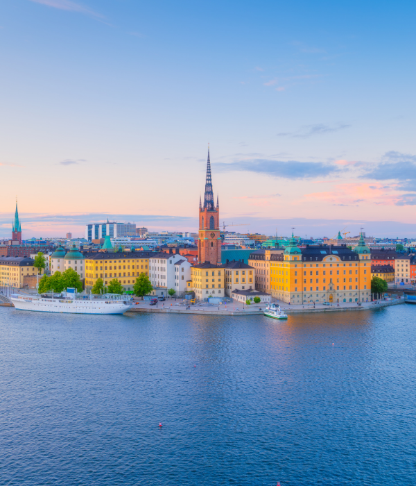 Colorful waterfront city skyline with church spires at sunset beside calm water