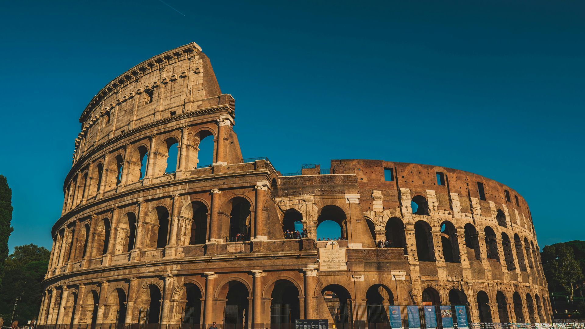Colosseum, Rome, Italy. Ancient amphitheater with arched openings against a clear, blue sky.