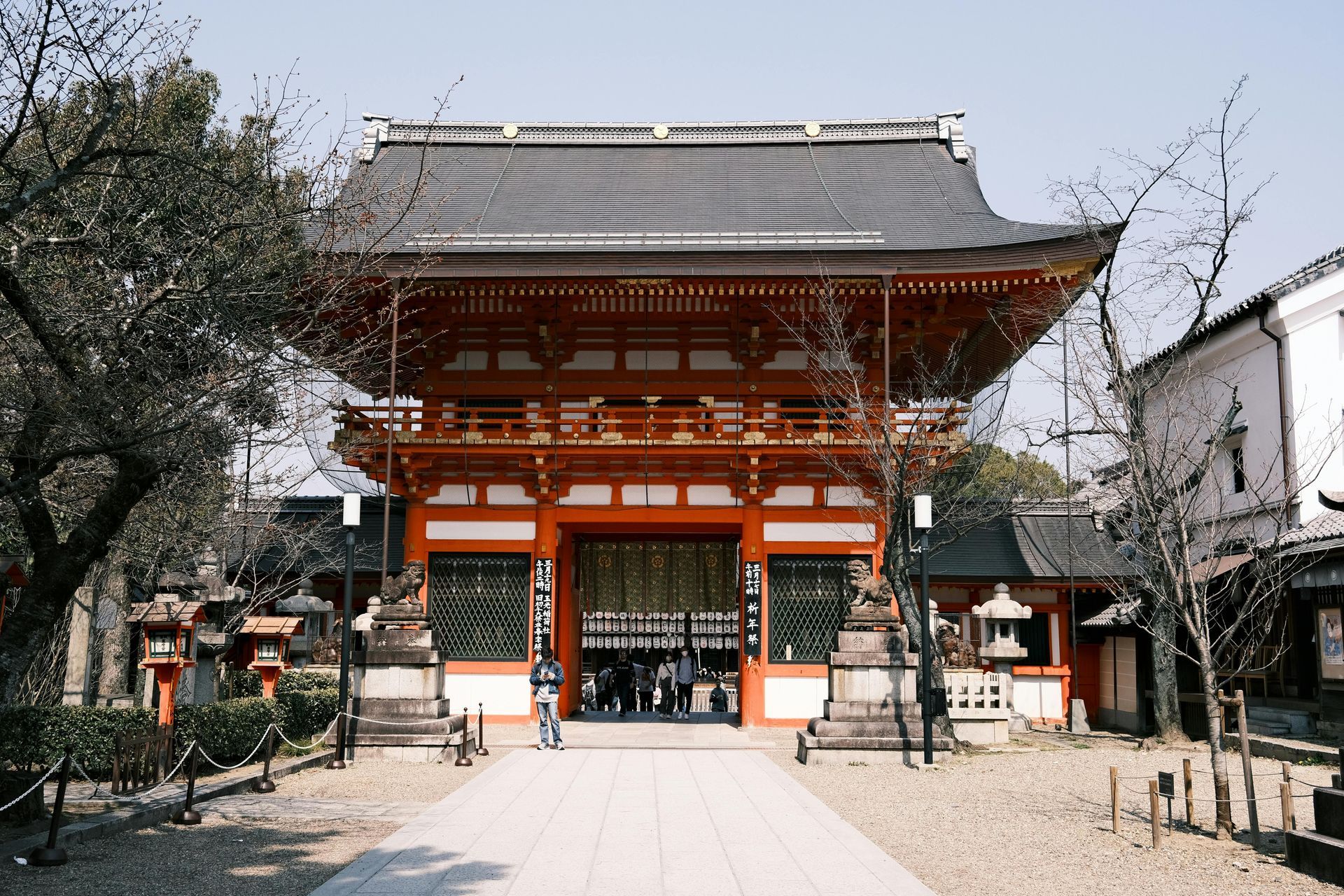 Red and black traditional Japanese temple with a tiled roof. People walk through its entrance.