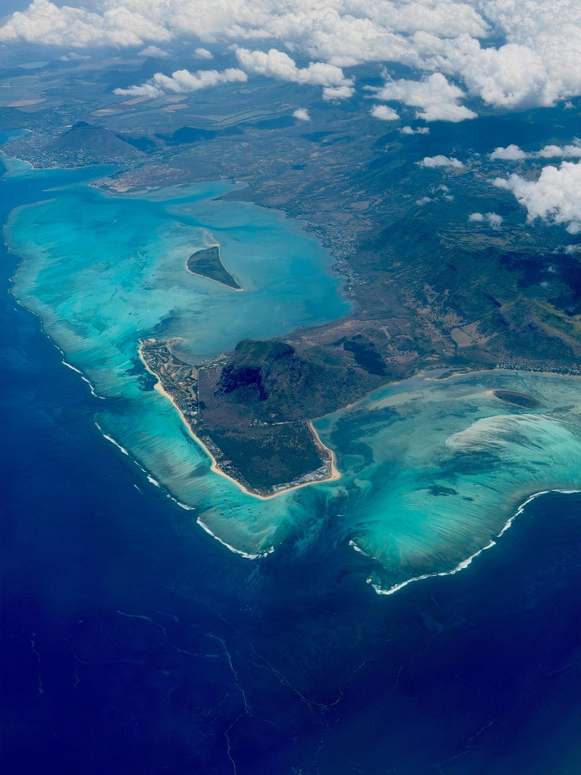 Aerial view of a tropical island with turquoise water, coral reefs, and a town.