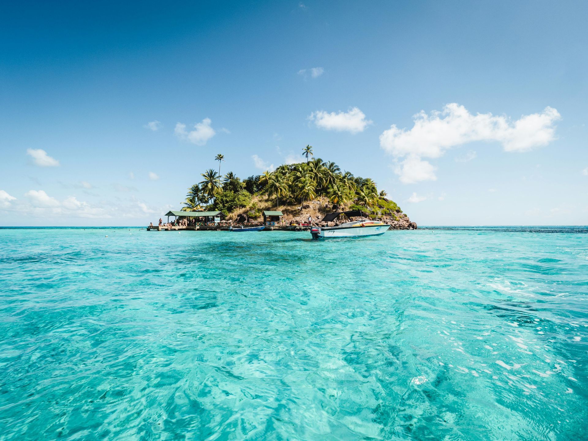 Small tropical island with lush green vegetation surrounded by turquoise water, under a blue sky.