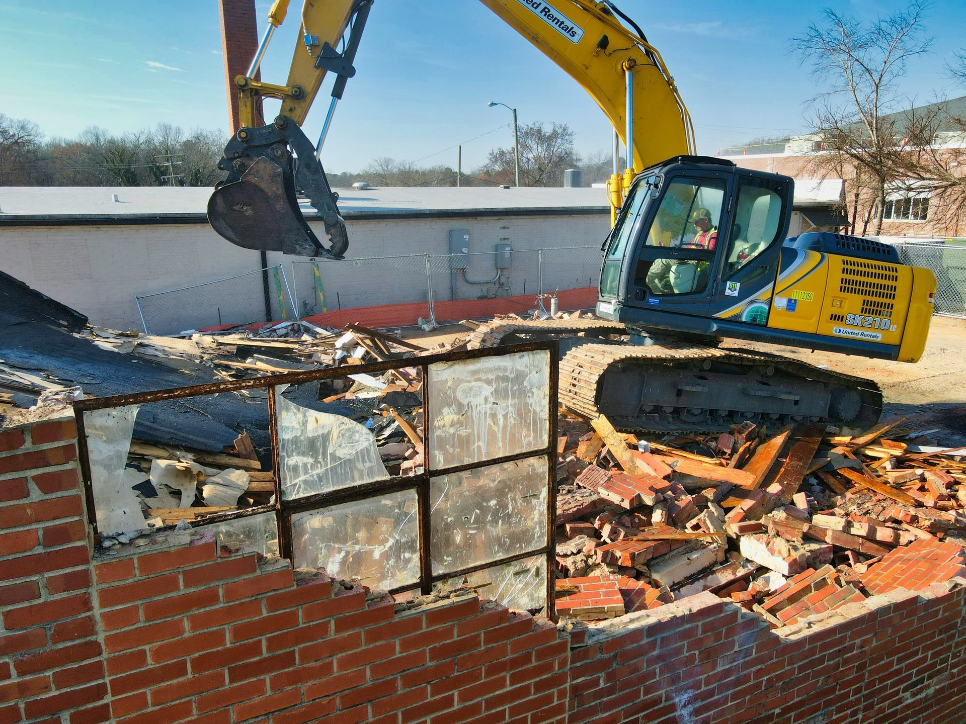 Excavator demolishing a brick wall amid rubble at a construction site