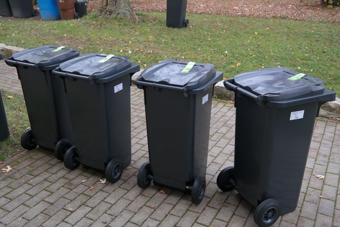 Garbage collector standing between blue and gray trash bins in an outdoor alley