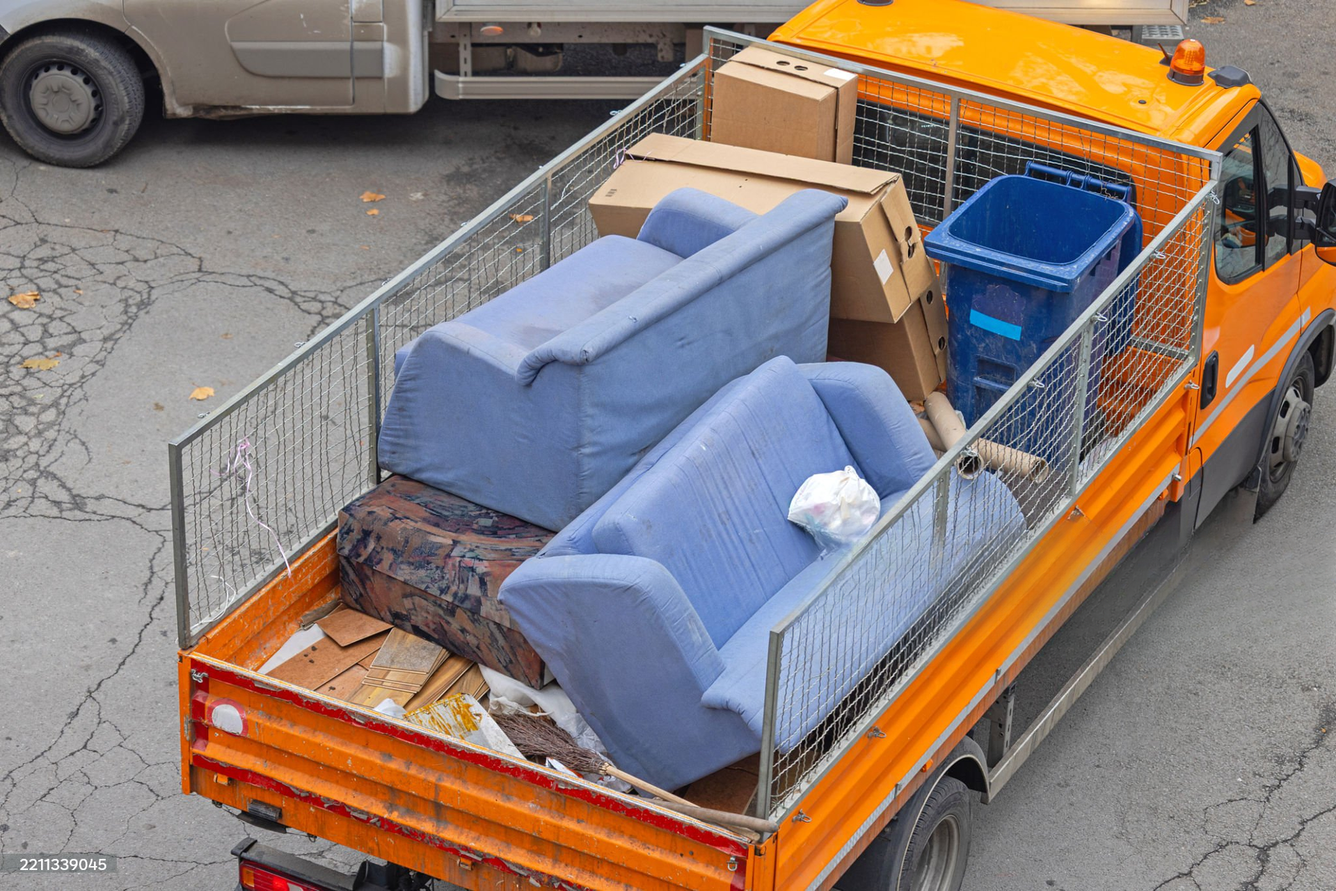 Garbage truck emptying waste into blue and yellow bins beside a brick building
