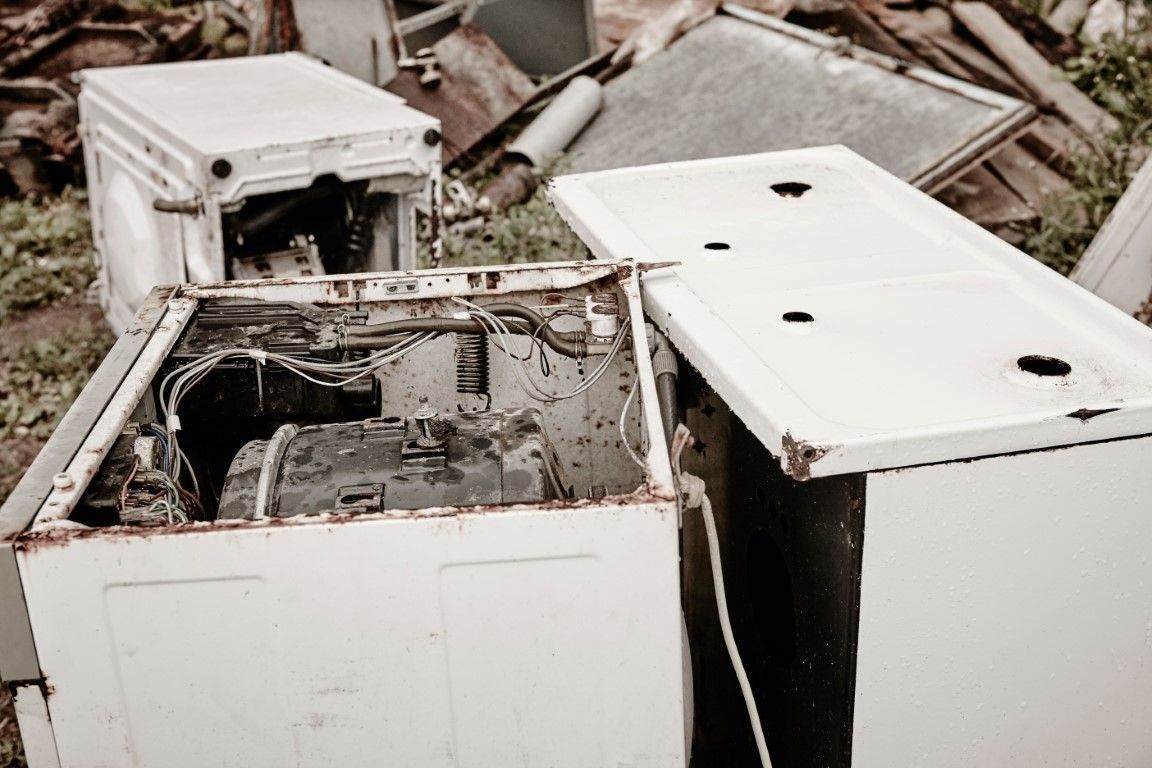 Damaged white appliances piled in debris, showing broken open metal components.