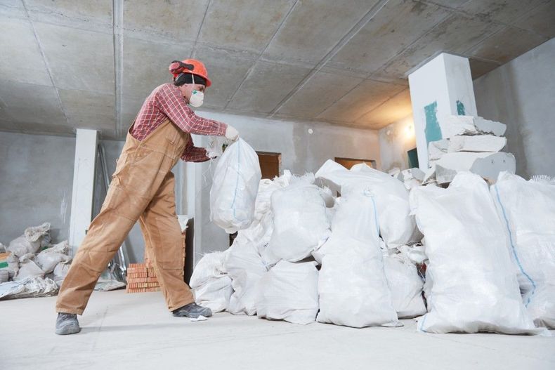 Worker in red cap stacking white bags in an unfinished concrete warehouse