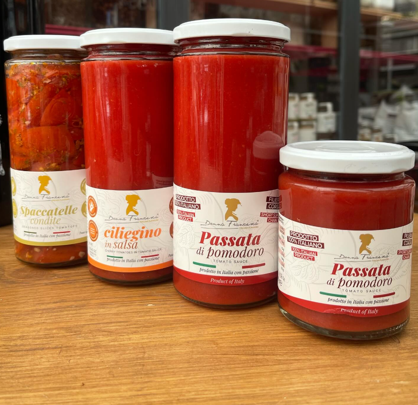 Quattro barattoli di salsa di pomodoro sono appoggiati su un tavolo di legno.