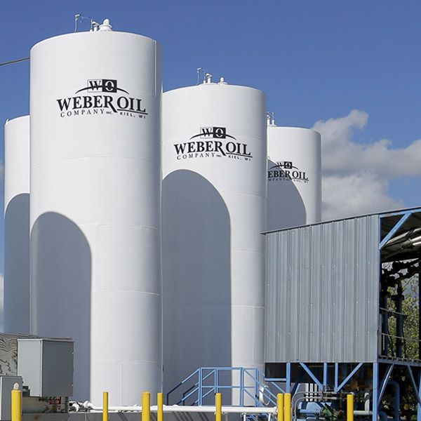 White Weber Oil storage tanks beside an industrial building under a blue sky