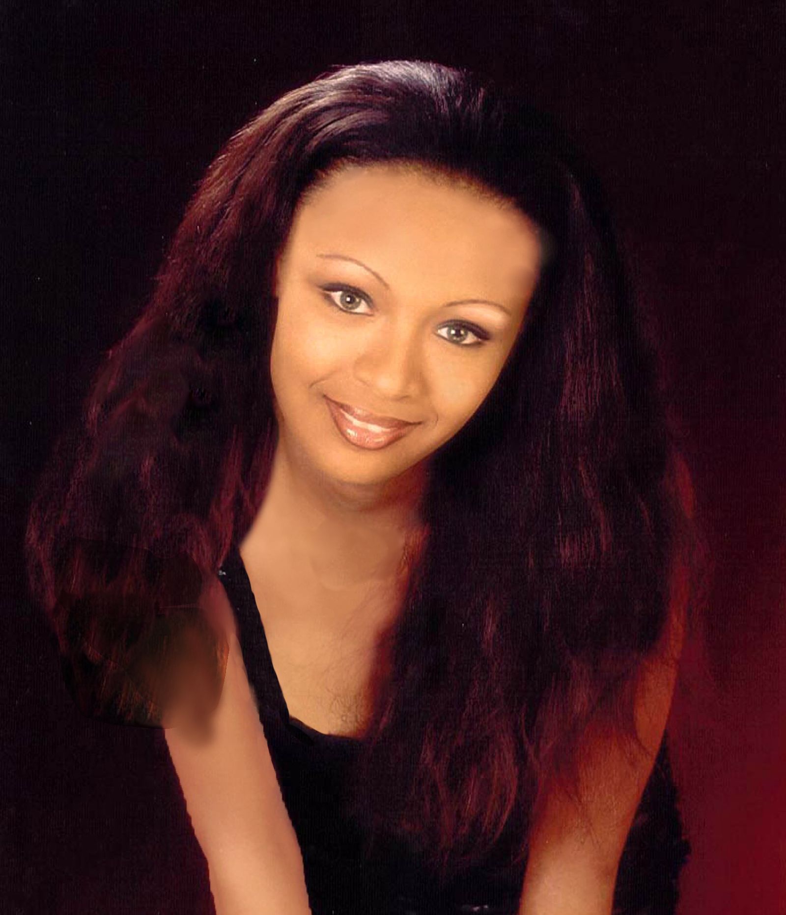 Studio portrait of a smiling woman with long dark hair against a black background