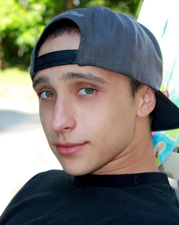 a young man wearing a baseball cap and a black shirt is looking at the camera .