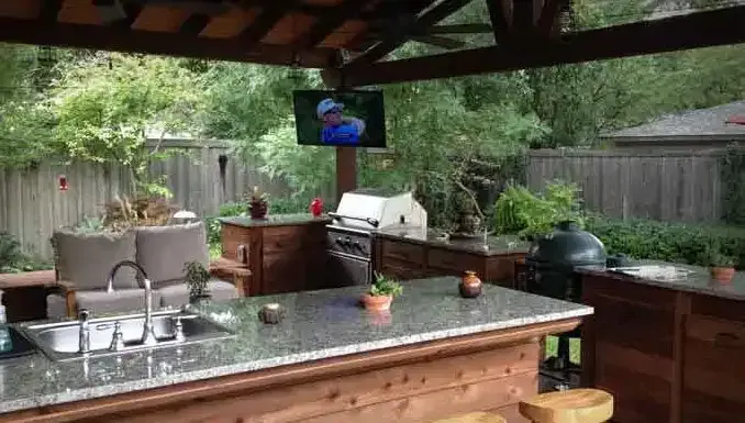 an outdoor kitchen with a sink , grill , television and a couch .