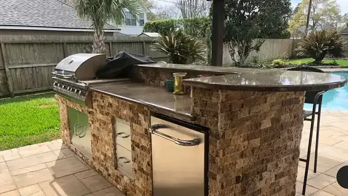 a large outdoor kitchen with a grill and stainless steel appliances is sitting next to a pool .