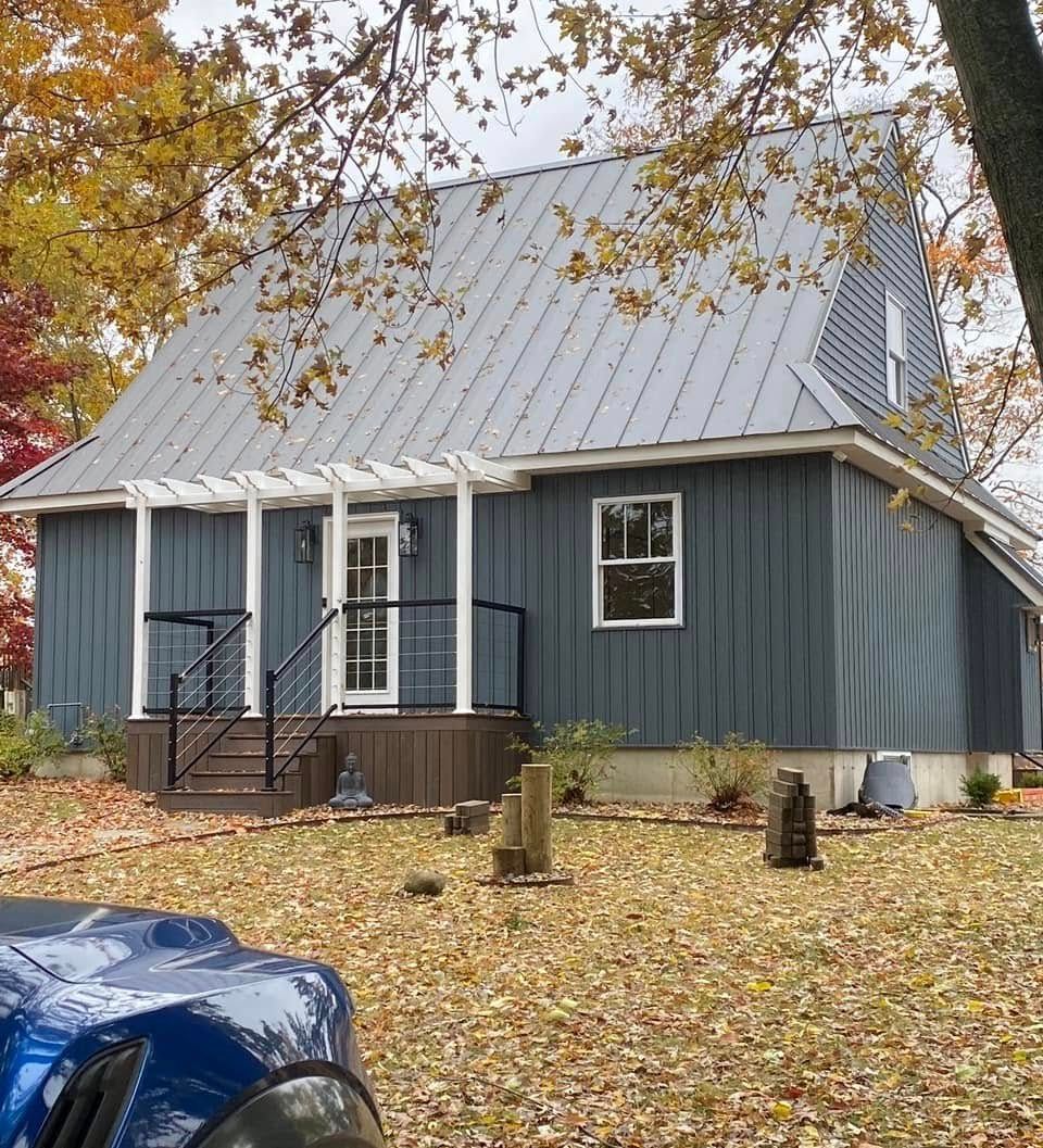 Blue-gray cabin with a metal roof amid autumn trees and fallen leaves