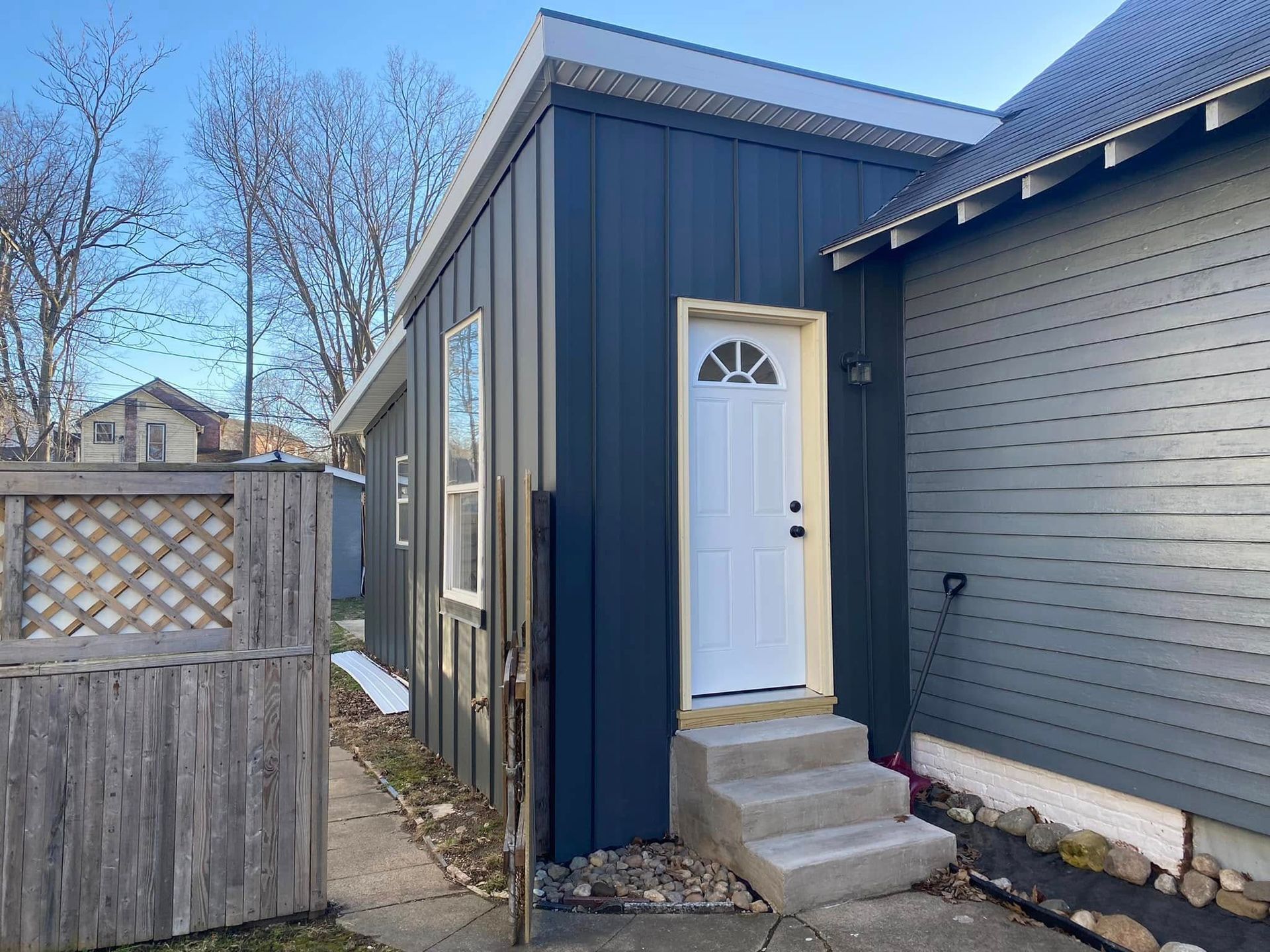 Blue house exterior with a white door, small concrete steps, and a wooden fence beside a gray wall