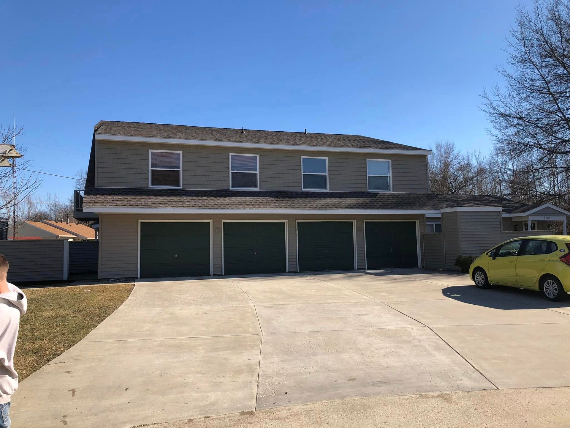 Two-story tan building with four garage doors and a concrete driveway under a clear blue sky