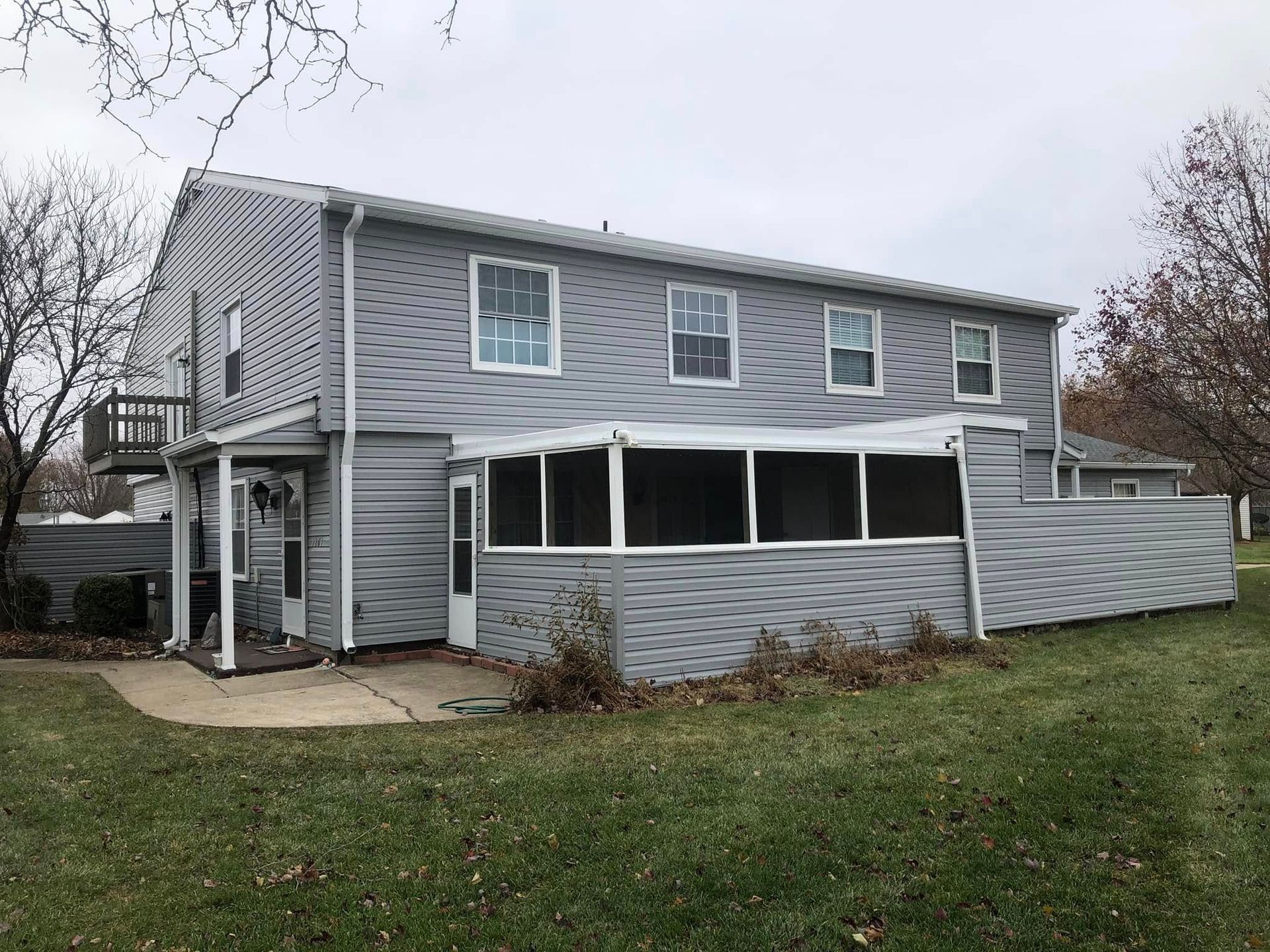 Gray two-story house with screened porch, deck, and grassy yard