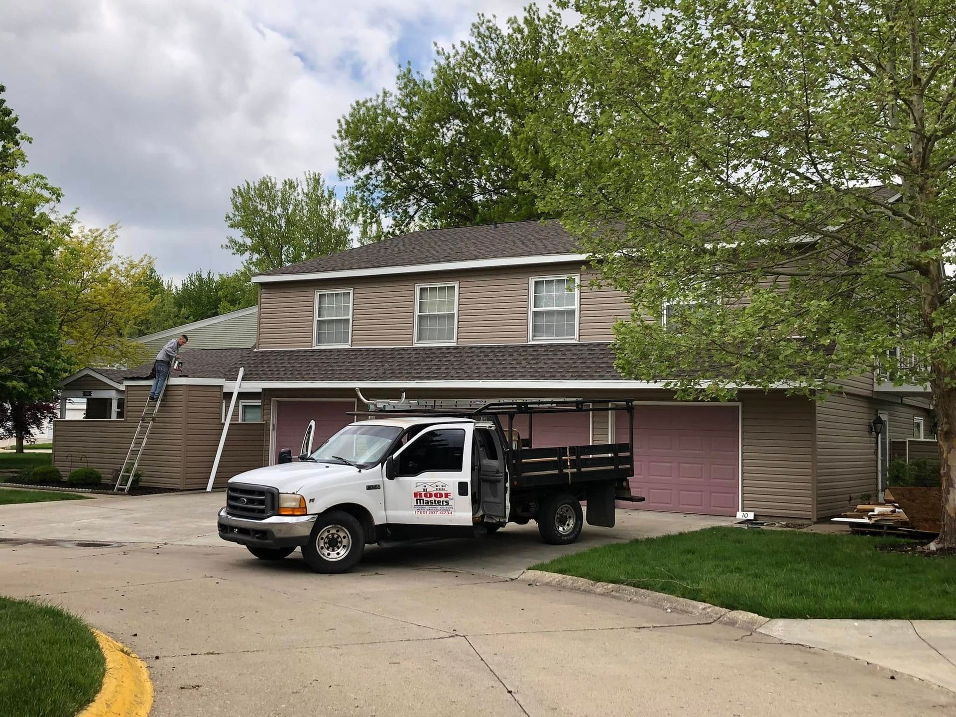 White pickup truck parked in front of a two-story house with a detached garage and trees in the yard