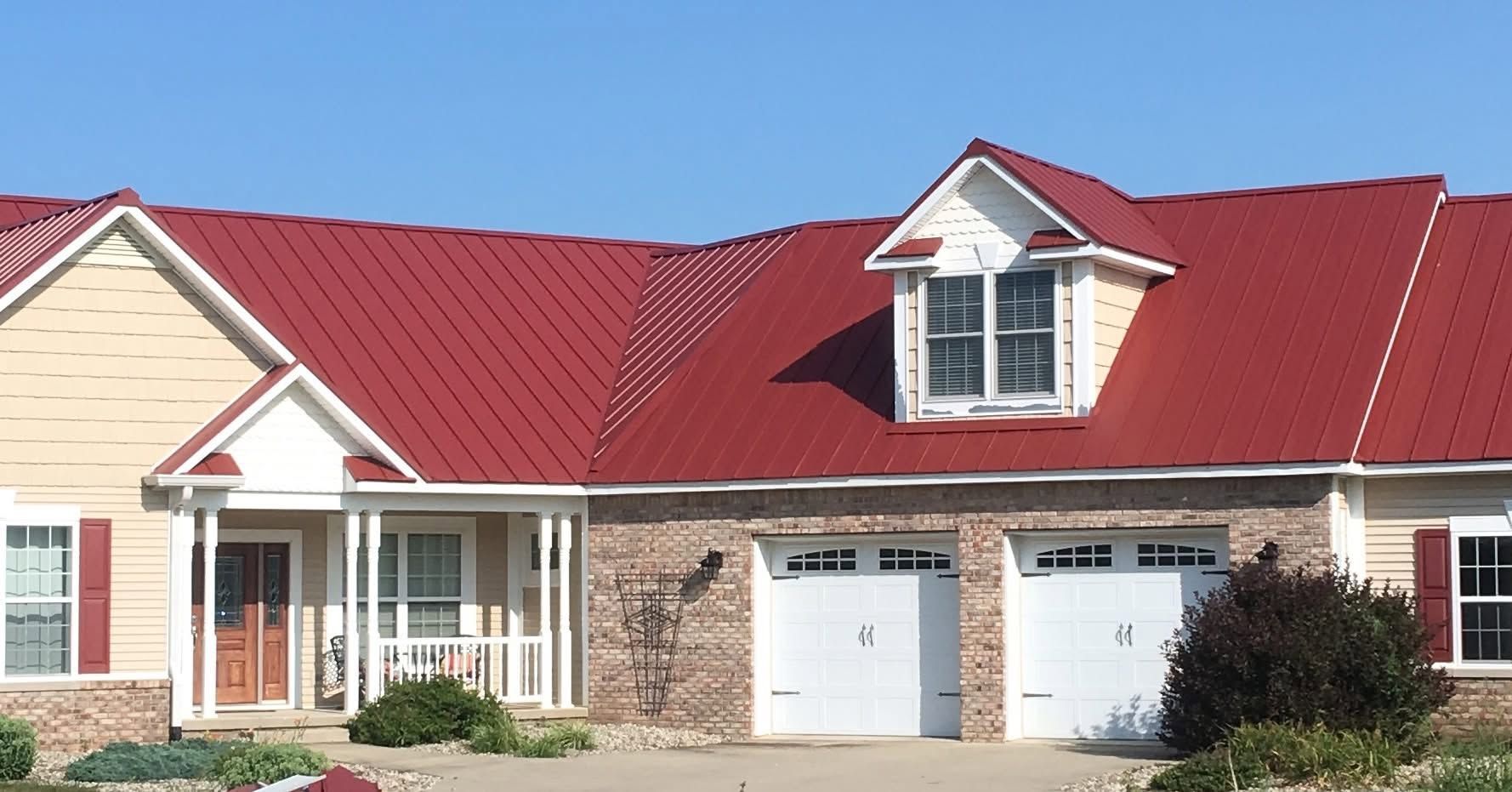 Brick house with a red roof and two white garage doors under a dormer window