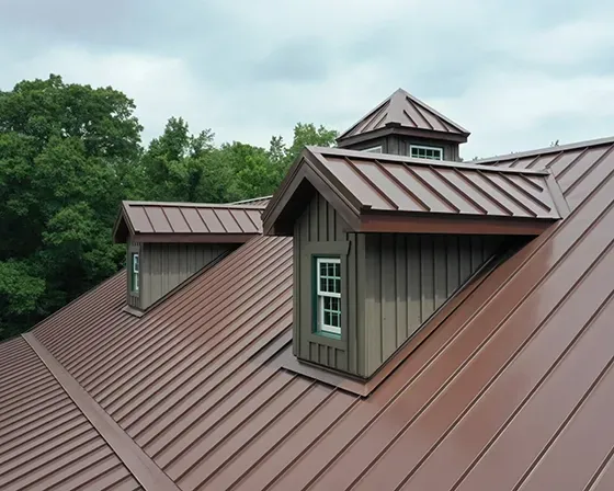 Brown metal roof with dormer windows on a house, surrounded by green trees under a cloudy sky