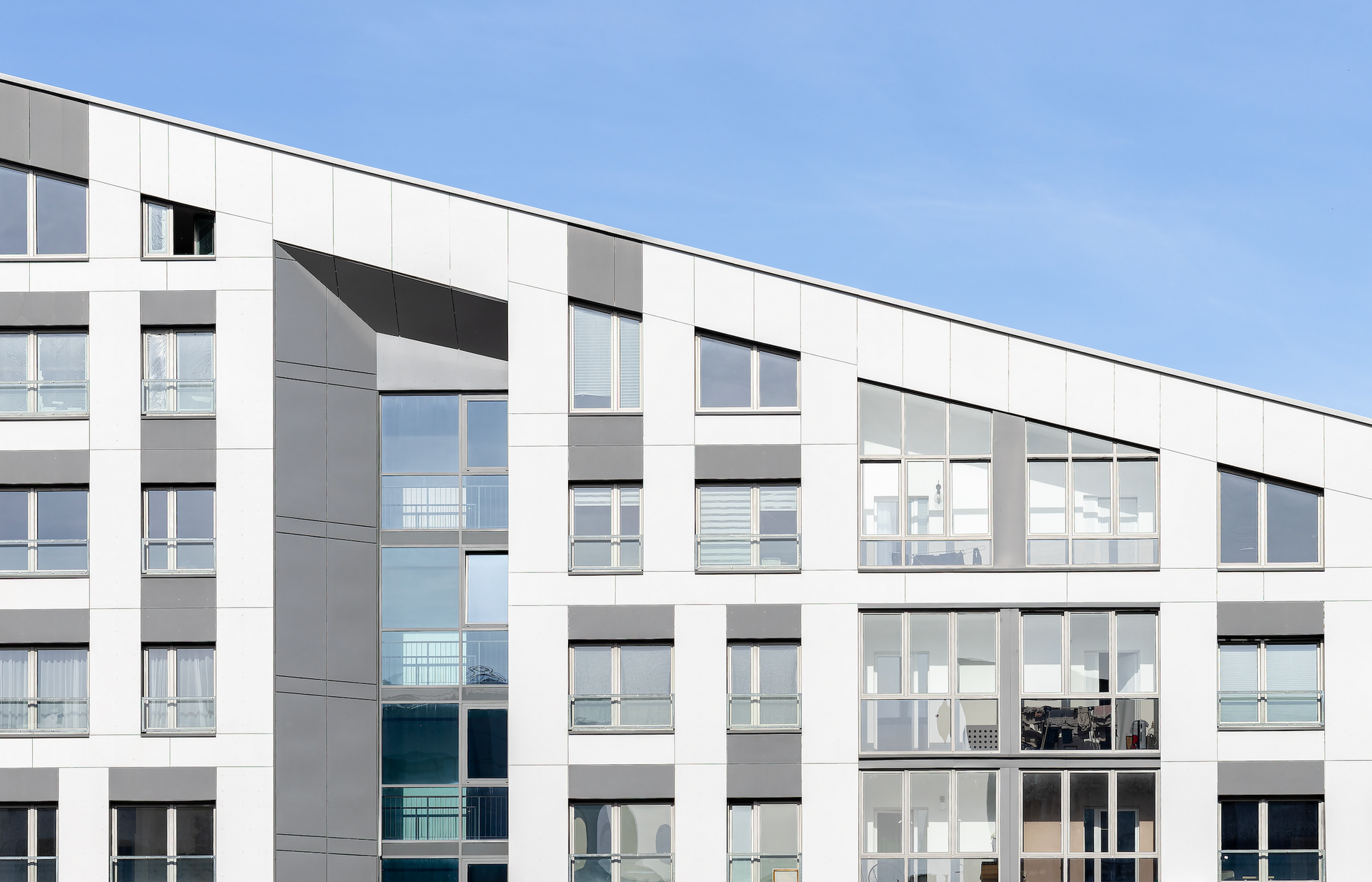 Modern white apartment building with large windows under a blue sky