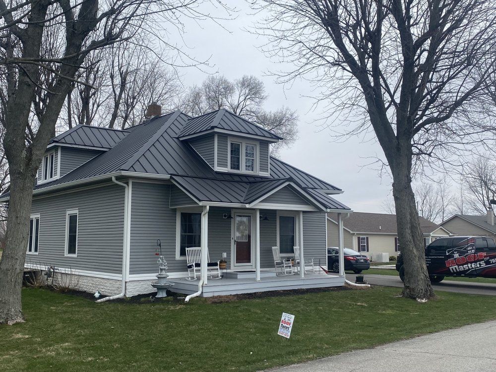 Gray two-story house with porch and dormer windows on a cloudy day, with a yard sign in front.