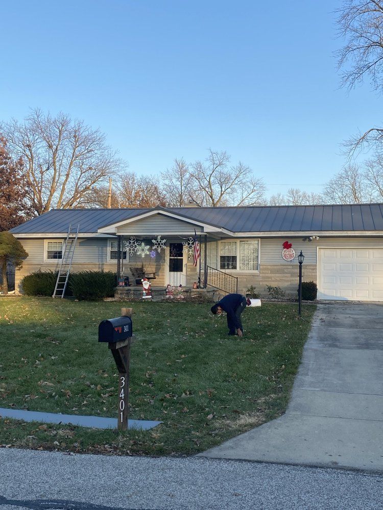 Suburban house with two people working in the front yard near a driveway and mailbox.