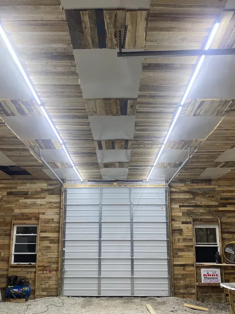 Interior of a rustic garage with wood-paneled walls, fluorescent lights, and a closed white roll-up door.