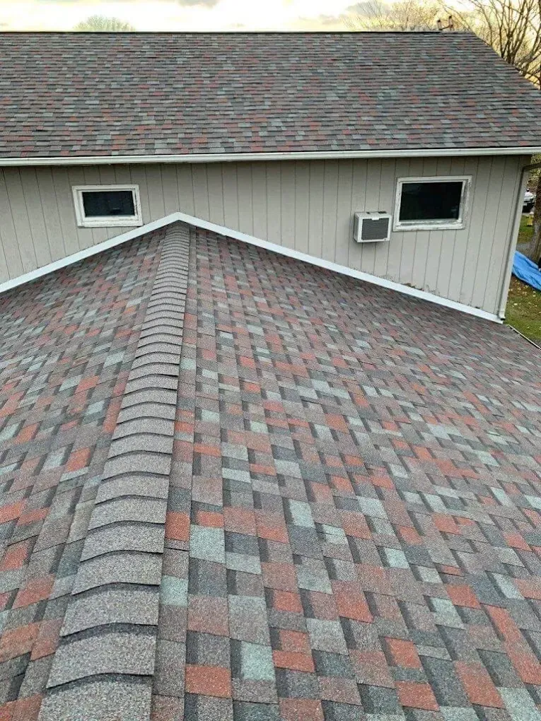 Rooftop view of gray and red shingle roofs on a house with beige siding and two windows